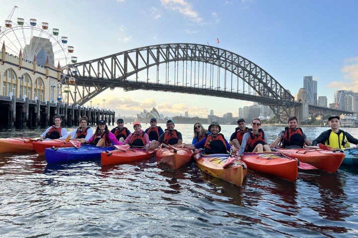 a group of people on a boat in the water with Sydney Harbour Bridge in the background