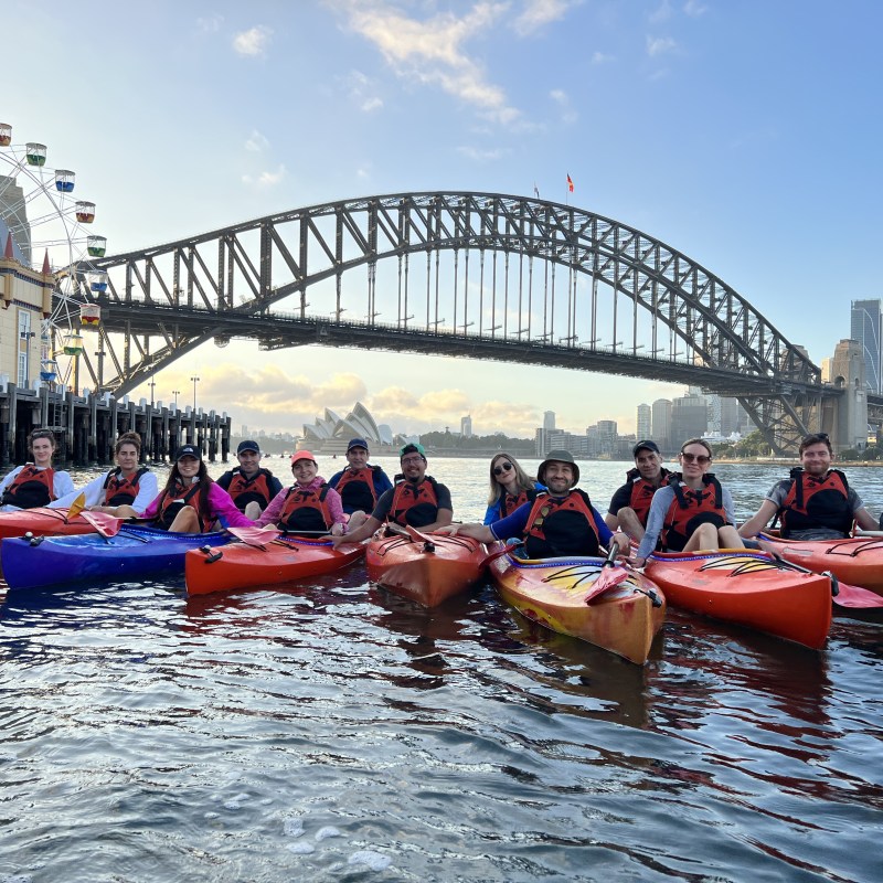 a group of people on a boat in the water with Sydney Harbour Bridge in the background