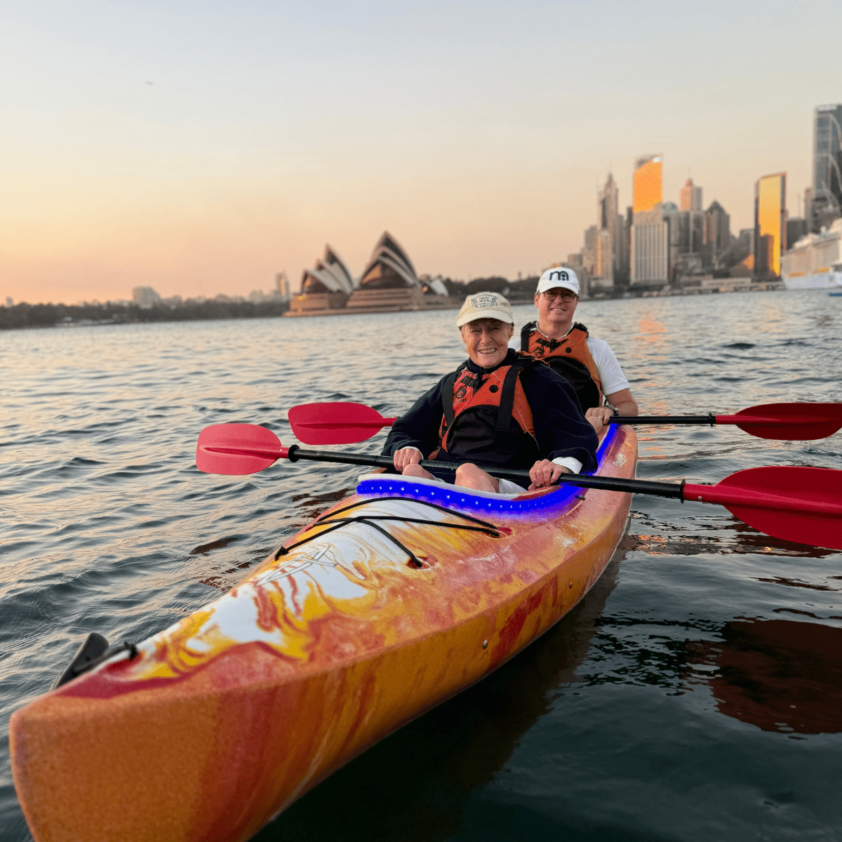Two people kayaking near Sydney Opera House at sunset.