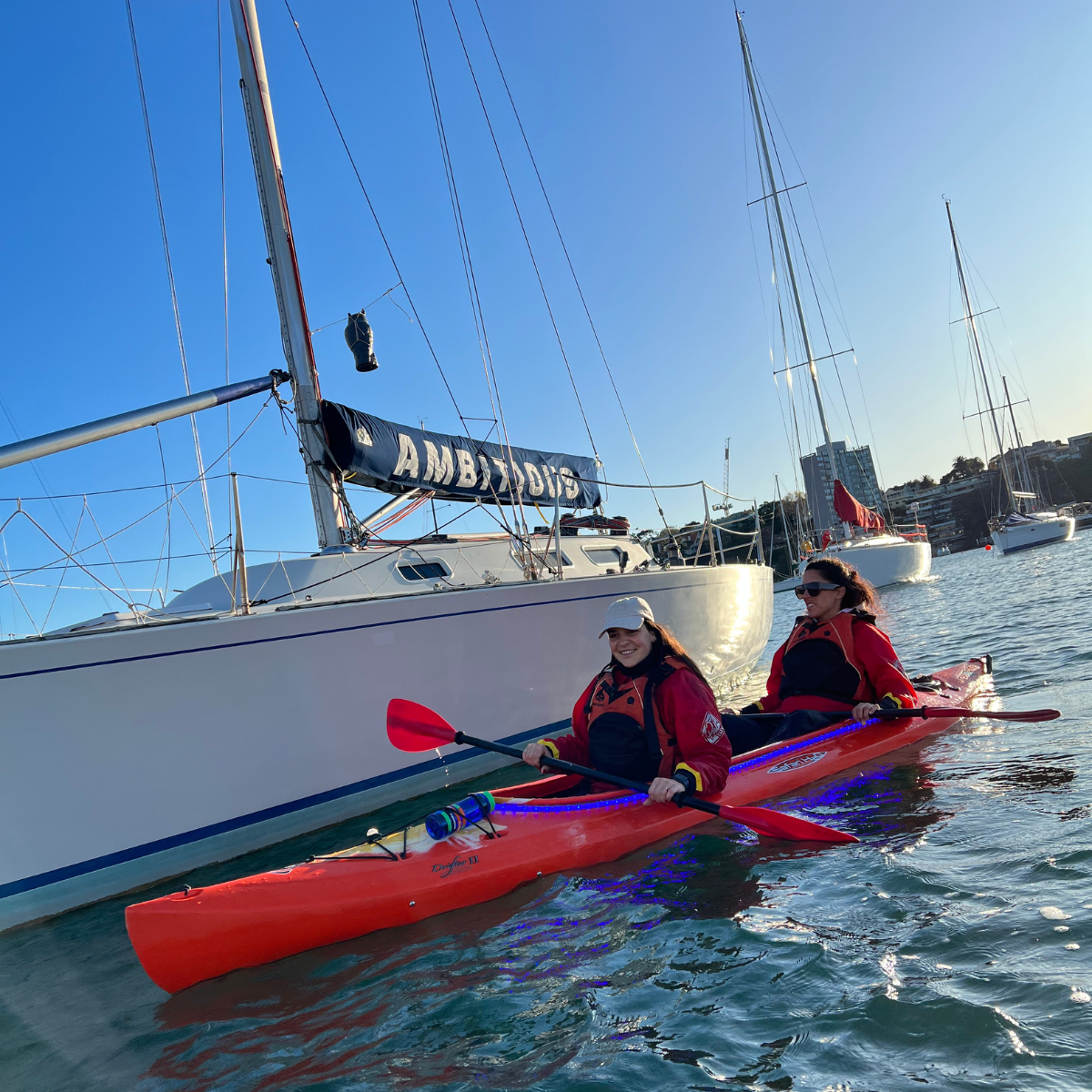 Two people kayaking near a large sailboat on a sunny day.