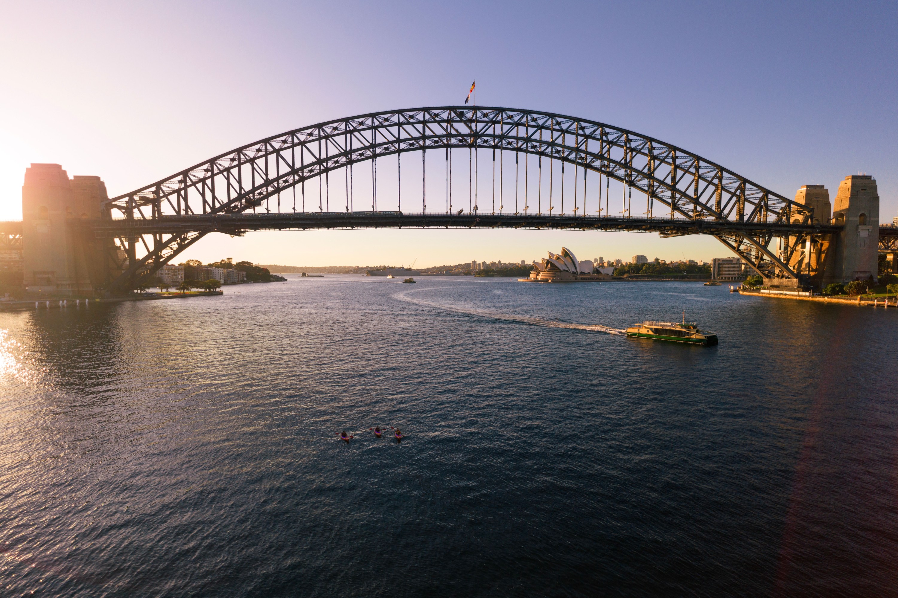 Sydney Harbour Bridge at sunset with ferry and Opera House in background.